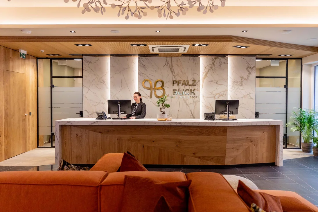 Ihr Hotel im Dahner Felsenland: Pfalzblick Wald Spa Resort Empfangstresen mit Angestellter in modernem Hotel mit Holz- und Marmordesign