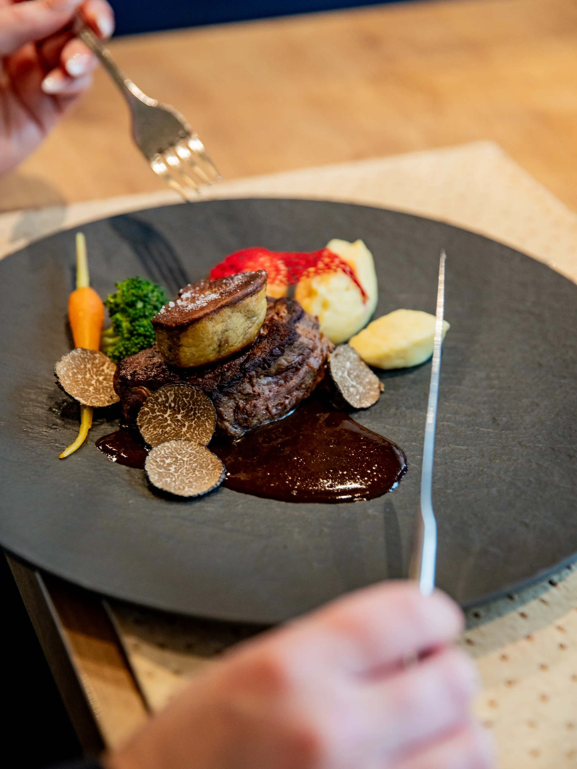 Ihr Hotel im Dahner Felsenland: Pfalzblick Wald Spa Resort Gourmetgericht mit Rinderfilet, Trüffelscheiben, Gemüse und Sauce auf schwarzem Teller