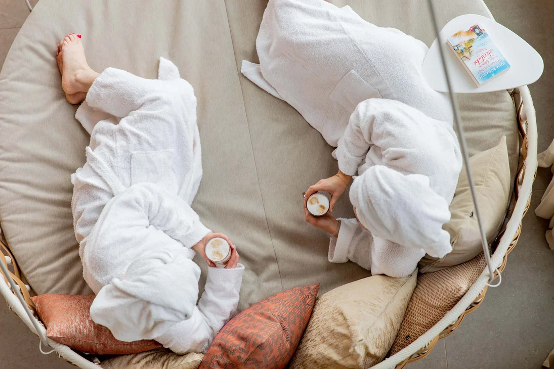 Ihr Hotel im Dahner Felsenland: Pfalzblick Wald Spa Resort Zwei Personen in Bademänteln trinken Kaffee und entspannen auf einem Sofa