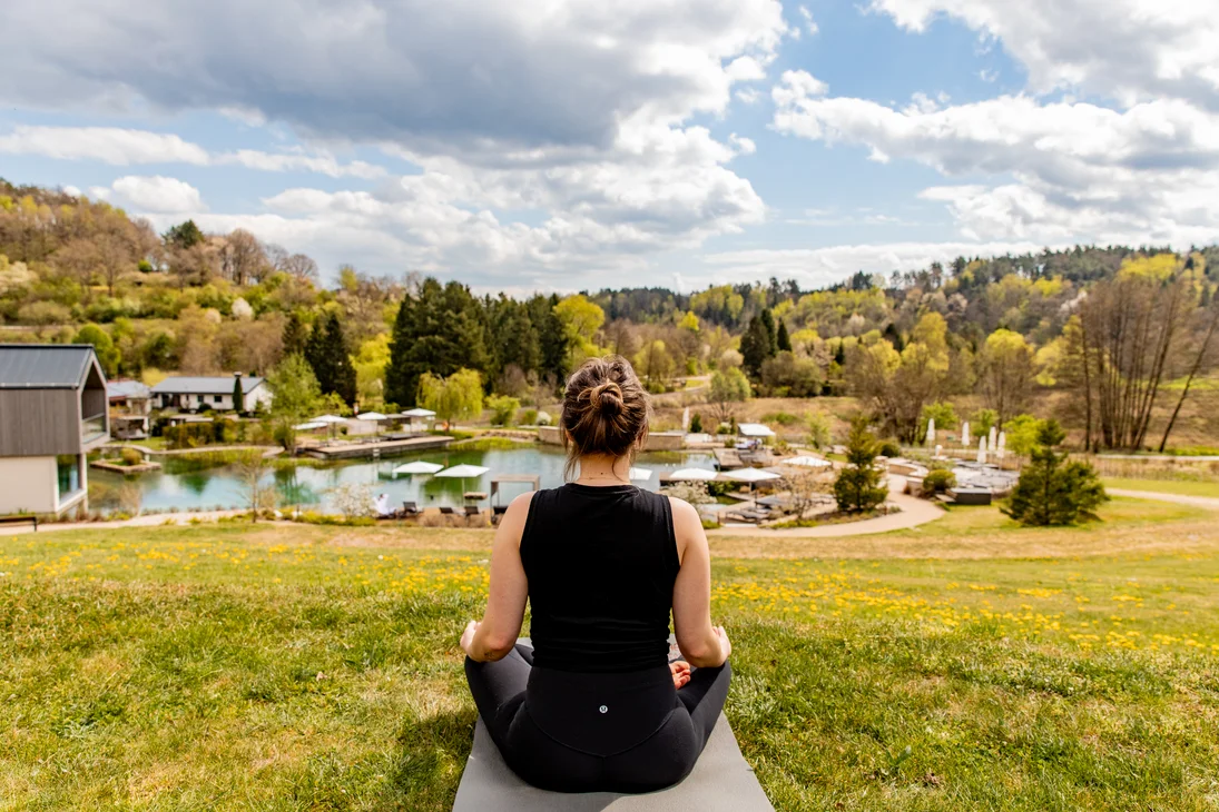 Ihr Hotel im Dahner Felsenland: Pfalzblick Wald Spa Resort Frau meditiert draußen mit Blick auf See und Wald im Frühling