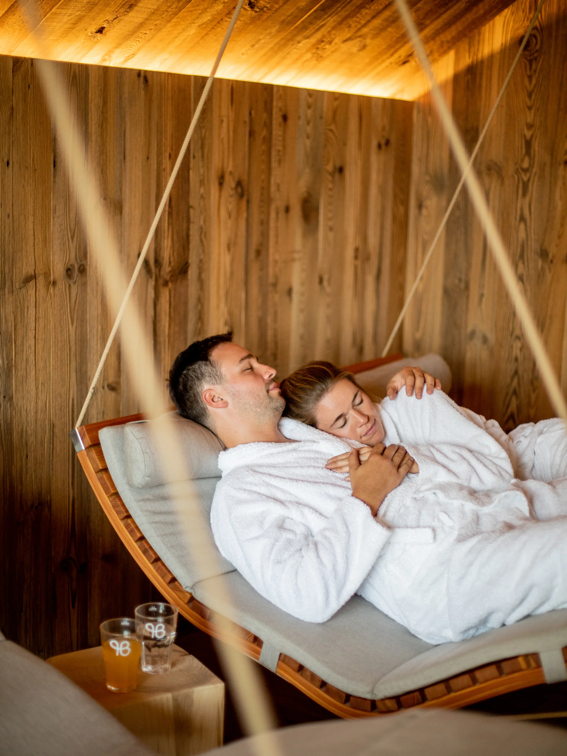 Ihr Hotel im Dahner Felsenland: Pfalzblick Wald Spa Resort Paar in weißen Bademänteln entspannt auf hängender Liege in Holzraum