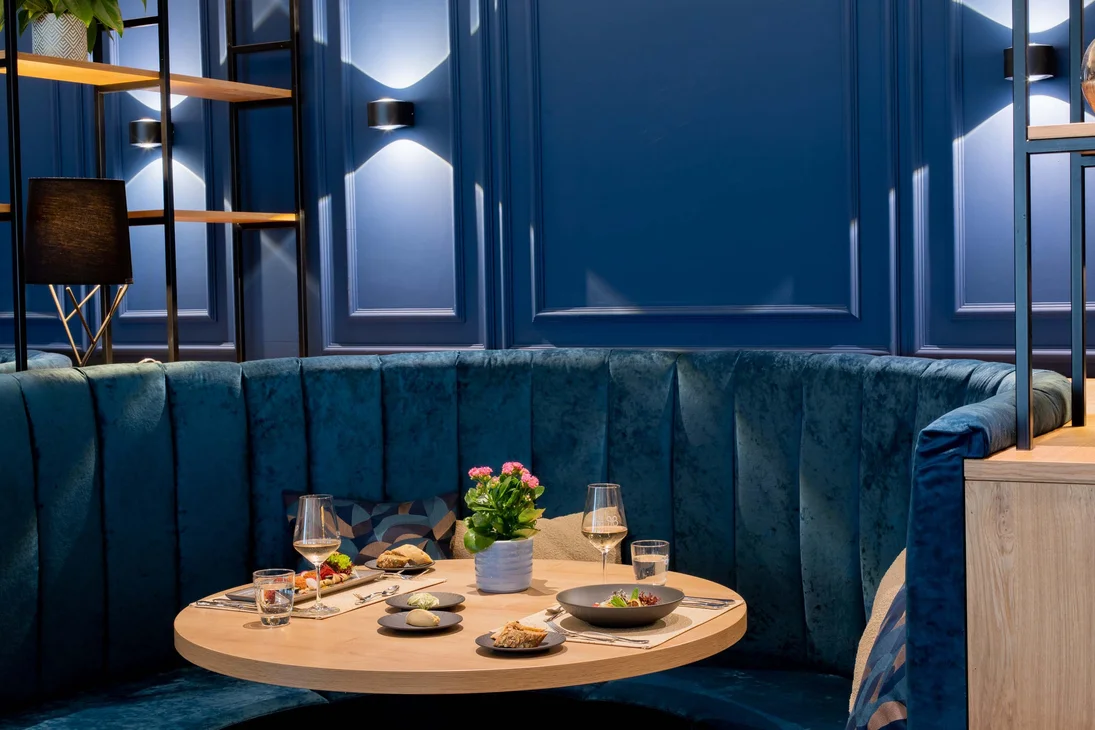 Ihr Hotel im Dahner Felsenland: Pfalzblick Wald Spa Resort Elegante Sitzecke mit rundem Holztisch und blauen Polstern im Restaurant