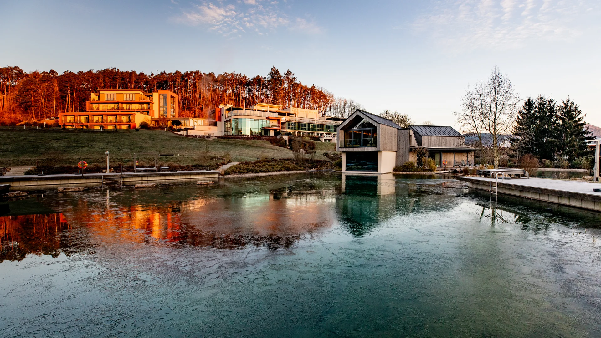 Ihr Hotel im Dahner Felsenland: Pfalzblick Wald Spa Resort Moderne Spa-Gebäude spiegeln sich im Außenpool vor einem bewaldeten Hang im Abendlicht