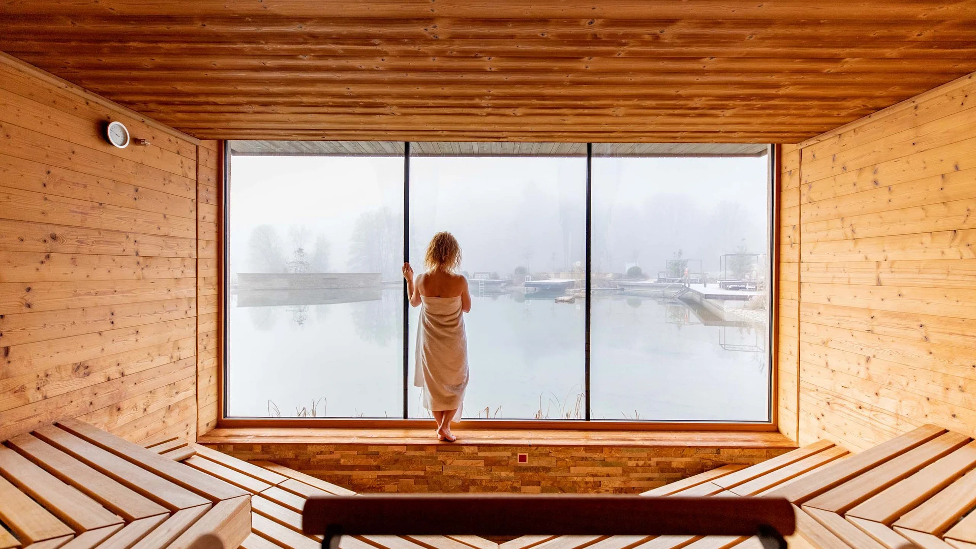Ihr Hotel im Dahner Felsenland: Pfalzblick Wald Spa Resort Frau in Handtuch blickt aus Sauna auf nebligen See