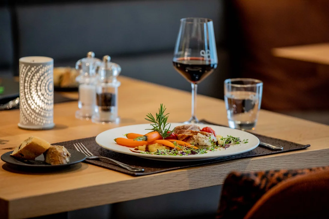 Ihr Hotel im Dahner Felsenland: Pfalzblick Wald Spa Resort Elegantes Restauranttischgericht mit Gemüse, Salz und Pfeffer, Rotwein und Kerze