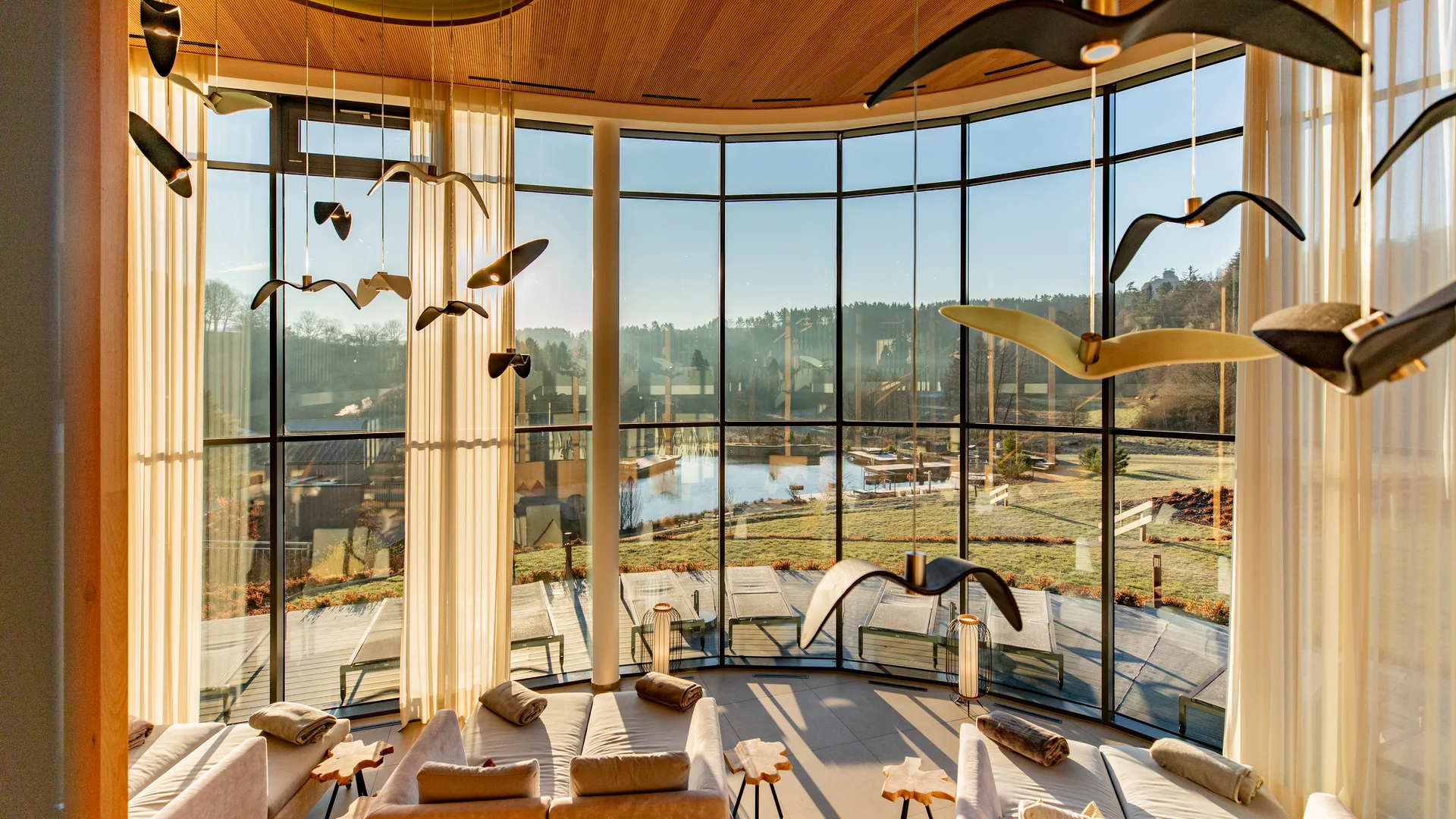 Ihr Hotel im Dahner Felsenland: Pfalzblick Wald Spa Resort Wohnzimmer mit großen Fensterfronten und Vogel-Deckendekoration