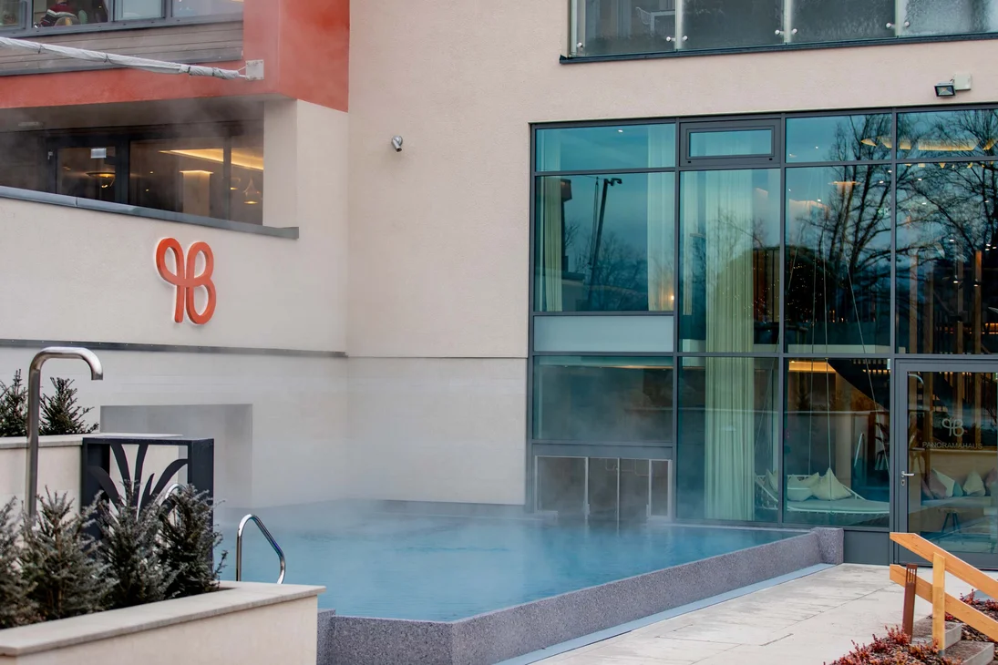 Ihr Hotel im Dahner Felsenland: Pfalzblick Wald Spa Resort Dampfender Außenpool neben modernem Gebäude mit großen Fenstern