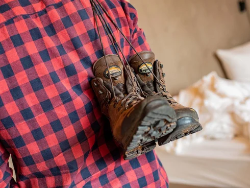 Blog – Neuigkeiten aus dem Pfalzblick Wald Spa Resort Wanderschuhe hängen über der Schulter einer Person mit rotem Karohemd