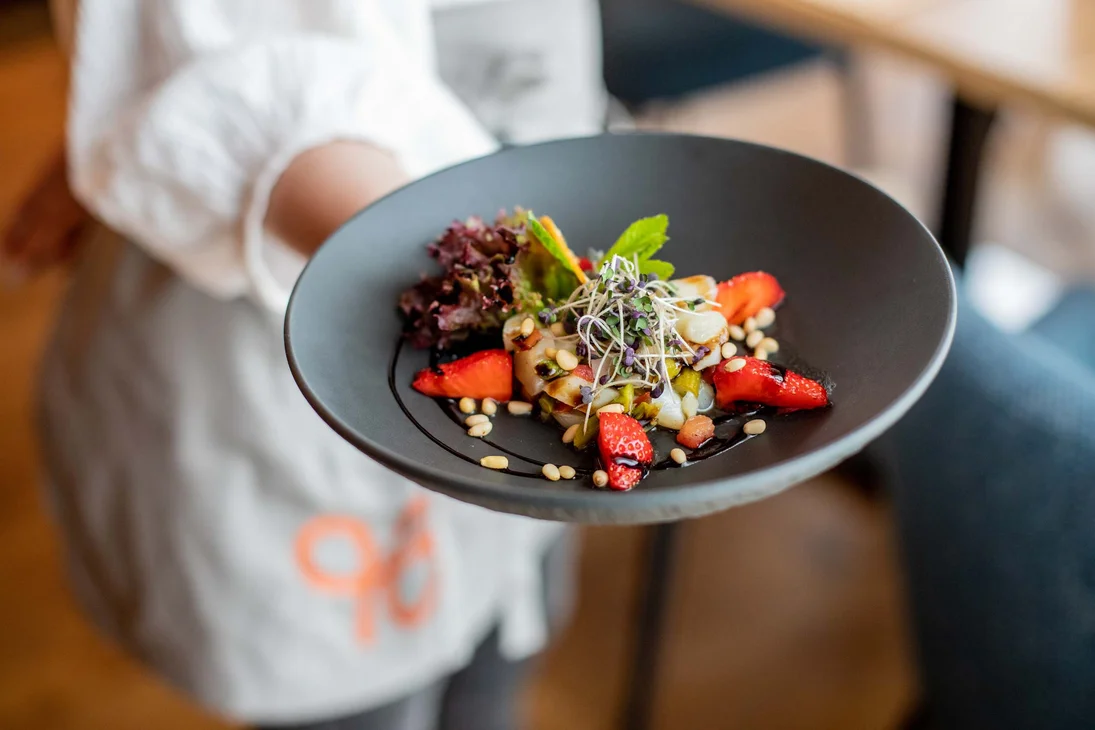 Ihr Hotel im Dahner Felsenland: Pfalzblick Wald Spa Resort Person hält schwarzen Teller mit Salat, Erdbeeren, Samen und grünen Kräutern