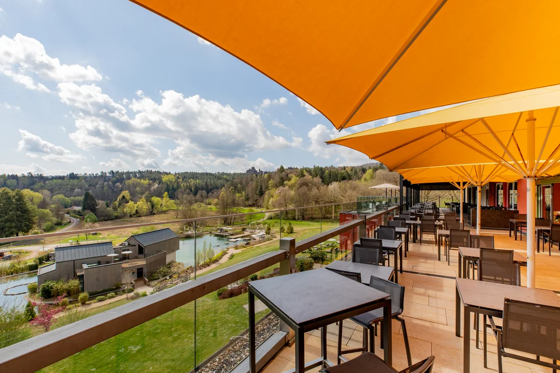 Ihr Hotel im Dahner Felsenland: Pfalzblick Wald Spa Resort Sonnige Terrasse mit Tischen und Stühlen mit Ausblick auf See und bewaldete Hügel